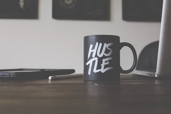 mug with hustle on it on desk with an open laptop, pad, pencil, ari monkarsh why entrepreneurs need accountability partners